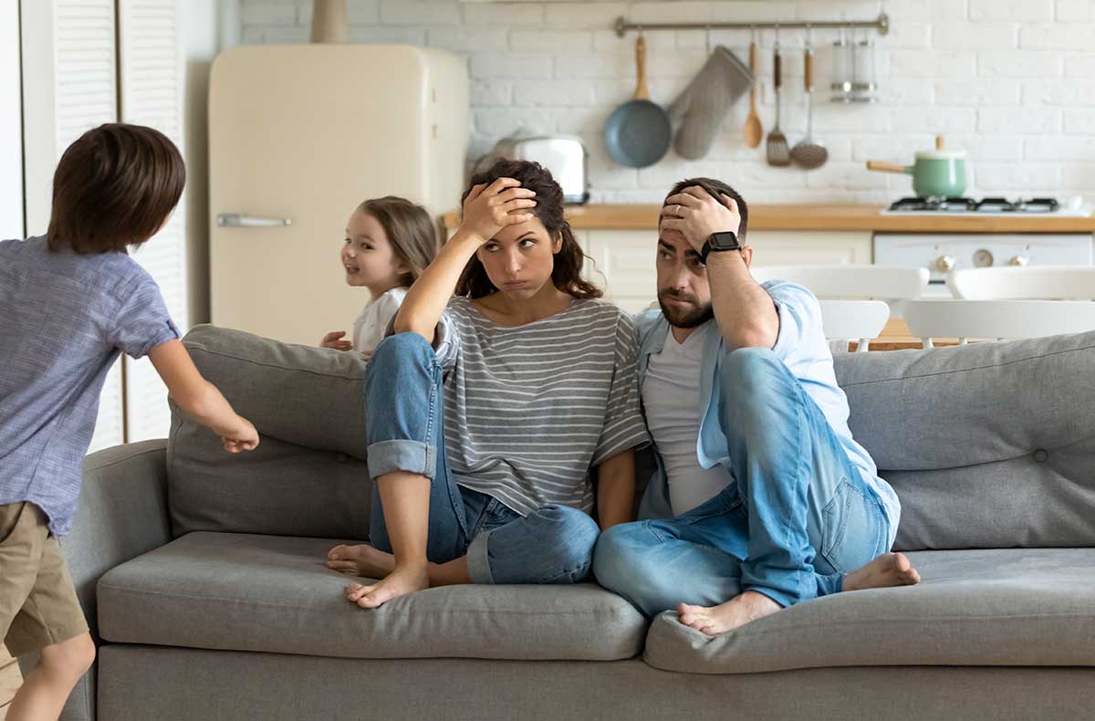 Exhasperated parents on couch watching out-of-control kids