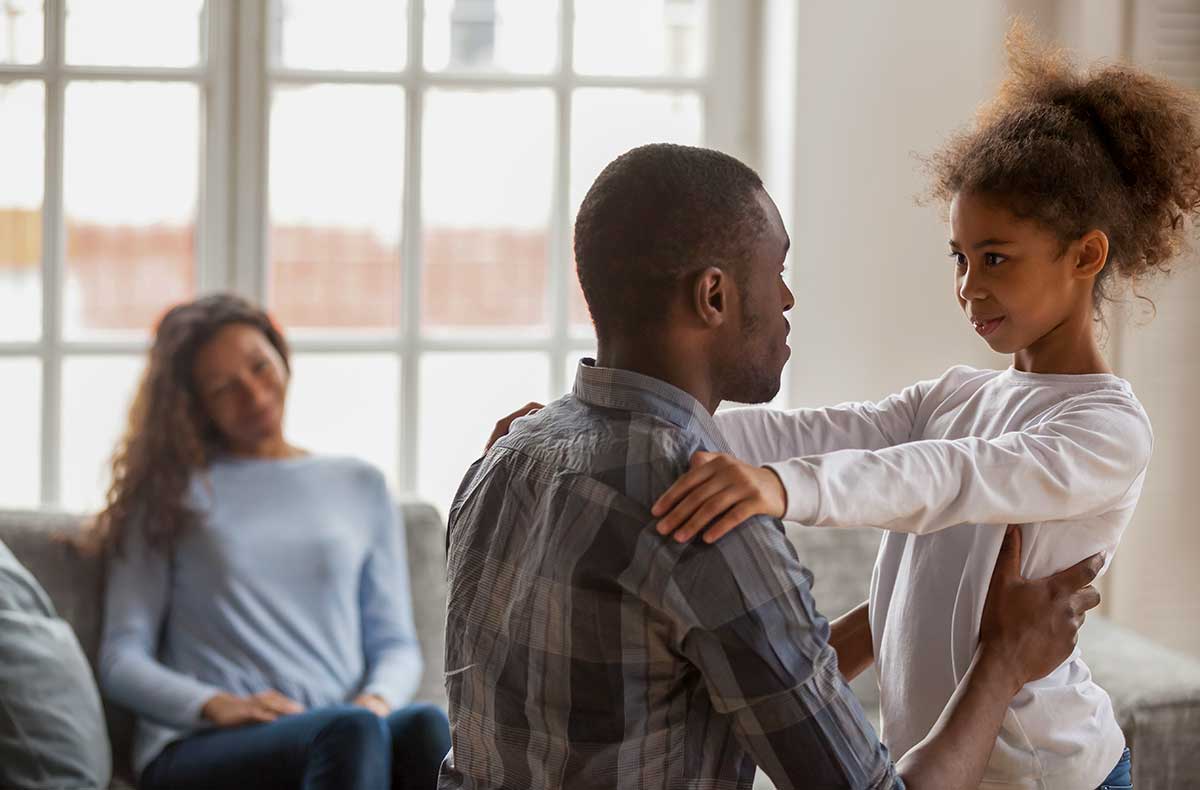 African-American man gently talking with his daughter while smiling mom looks on