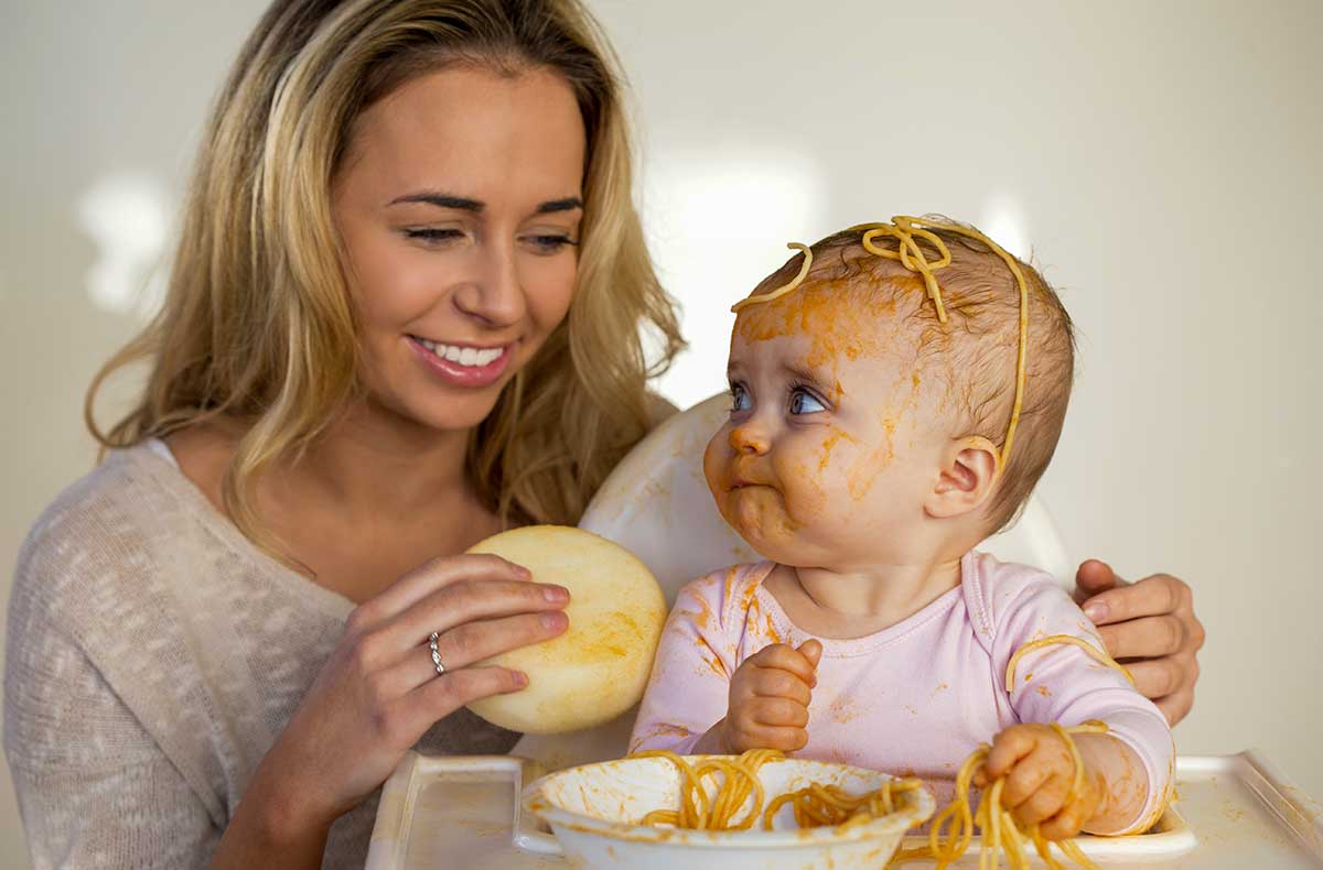 Mother feeding a baby with spaghetti all over it
